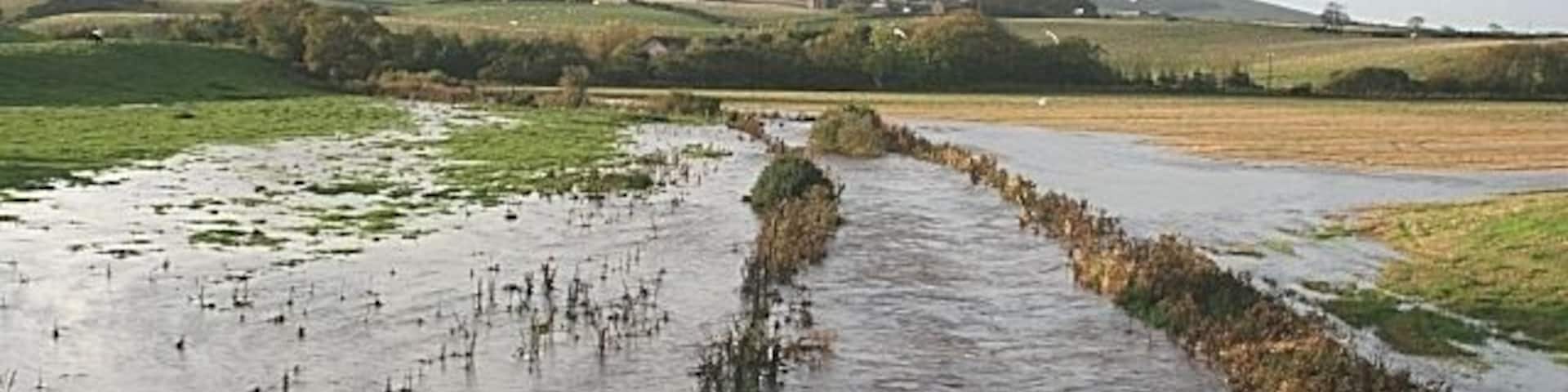 Flood at Rathen The burn here was in spate after several days of heavy rain. In the distance is Mormond Hill.
