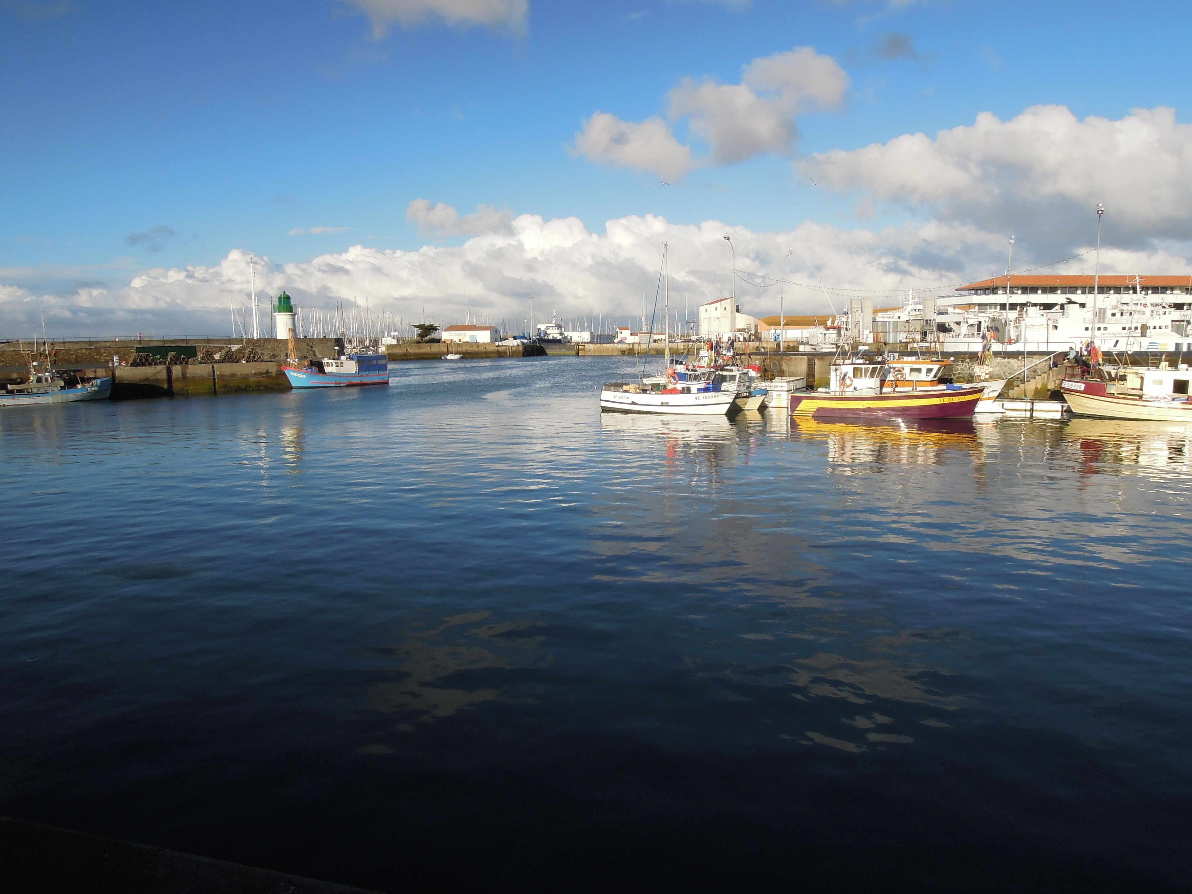 A harbor with several boats docked, a lighthouse, and a building with a red roof.