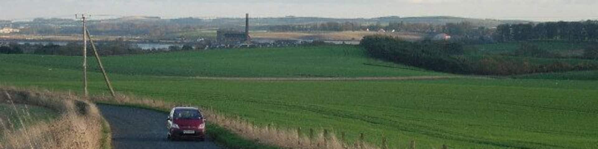 Minor road linking Balmullo and Leuchars. The view is east south east along the road from the north of the grid box. The chimney of the paper mill at Guardbridge is visible in the distance.