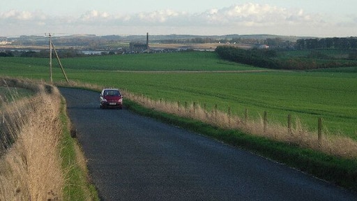 Minor road linking Balmullo and Leuchars. The view is east south east along the road from the north of the grid box. The chimney of the paper mill at Guardbridge is visible in the distance.
