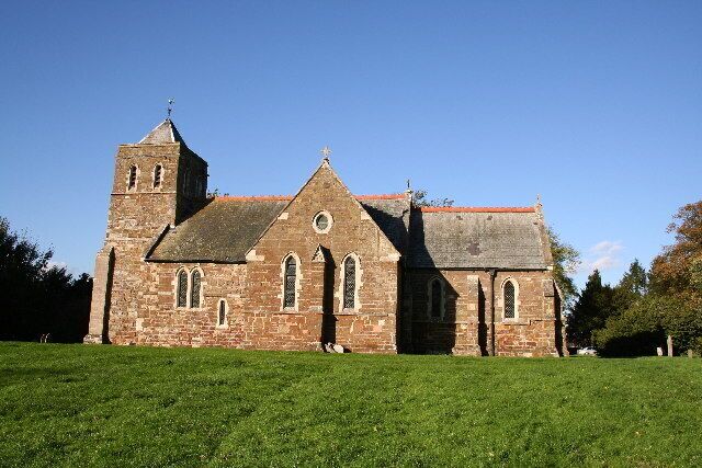 A historic stone church with a bell tower and a grassy field in the foreground.