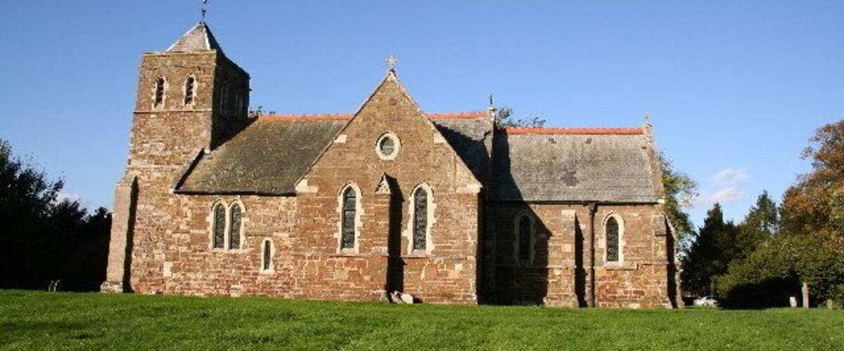 A historic stone church with a bell tower and a grassy field in the foreground.