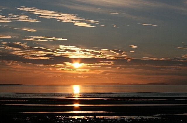 Un atardecer sobre una playa, con el sol reflejándose en el agua.