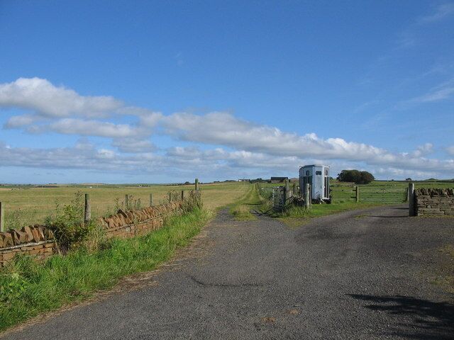 A rural road with a white building and a gate.
