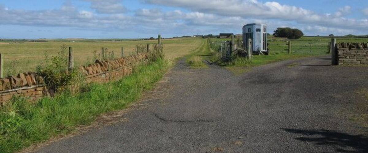 A rural road with a white building and a gate.
