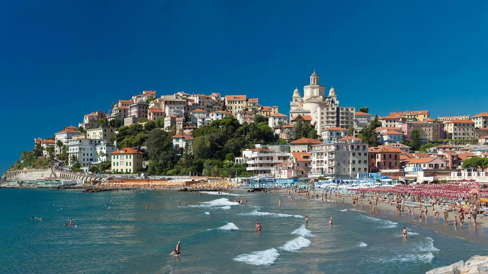 A coastal town with a beach, people swimming, and a prominent church on a hill.
