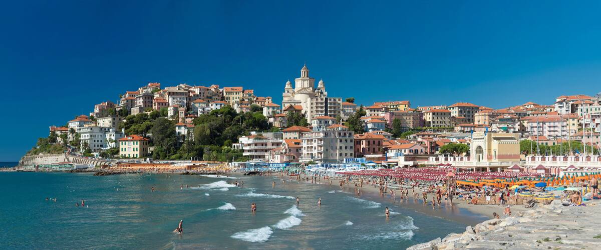A coastal town with a beach, people swimming, and a prominent church on a hill.