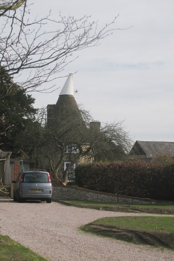 A gravel driveway leading to a white conical structure, possibly a church, with a car parked nearby.