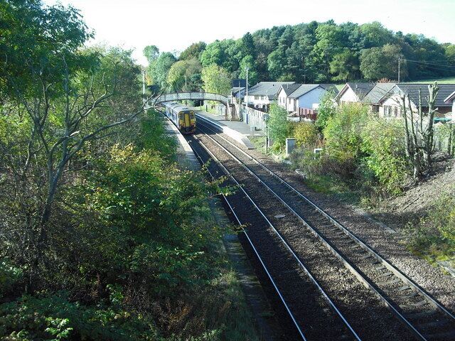 A train on tracks with a bridge, houses, and trees in the background.