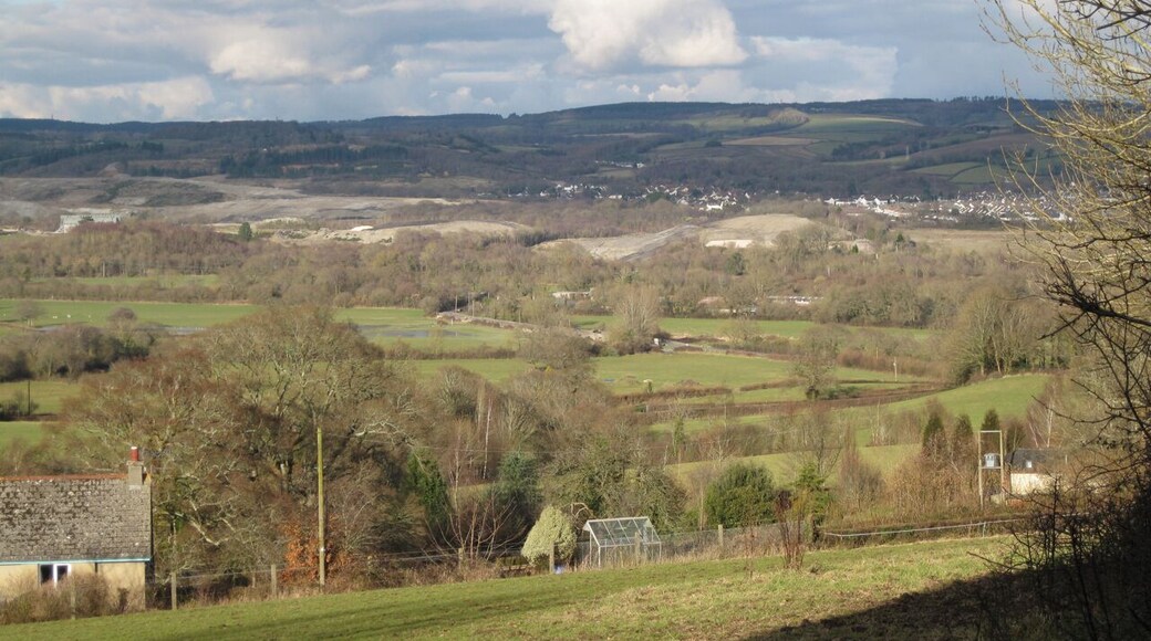 View of the Bovey Basin from Whitehill Road (3/3) Looking northeast over Higher Loady Park from below the cottages 1729963. In the middle distance are floodmeadows on the west bank of the Teign, crossed by the racetrack which is the old Exeter Road. In the centre of the photo, hidden by trees, is Teign Bridge. Left of centre is a mound of clay waste being formed on the east side of Denistone Quarry SX8574, with a wooded mound of old waste appearing to its left SX8573. Clay waste stretches away to the north. Right of centre the Broadway clay pit is being filled, with a big shaped mound to its right. Beyond it at some distance is Higher Sandygate SX8674, mostly. Between the mounds in the centre of the photo is the narrow wooded cleft which marks the course of the Abb Brook or Abbrook which, in its upper reaches, is the Ugbrooke Stream SX8676.
