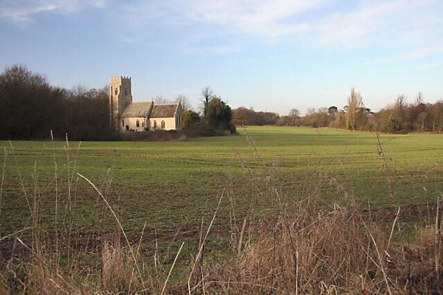A church with a tower, surrounded by a grassy field and trees.