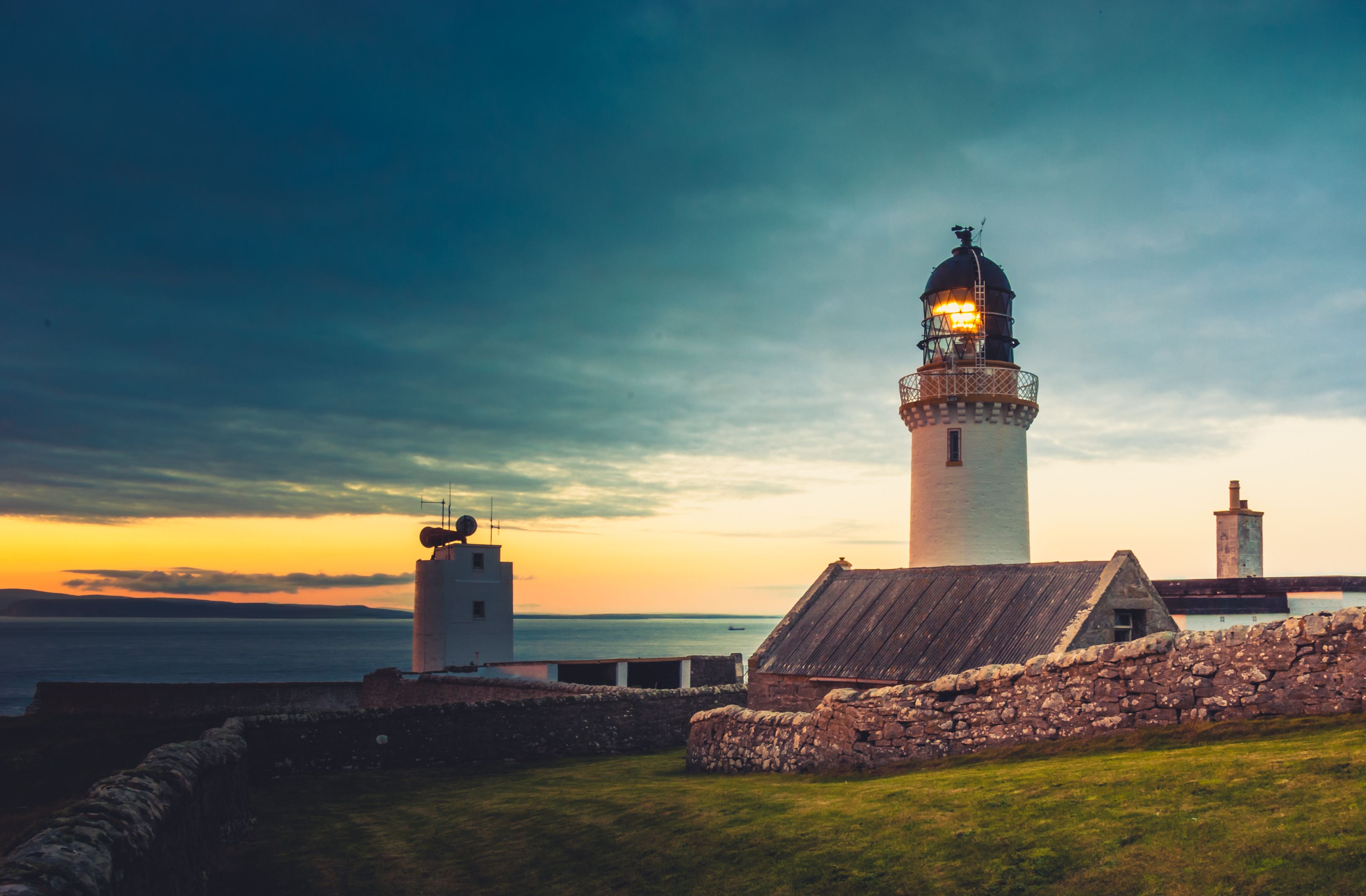 A lighthouse at sunset with a clear sky and calm sea.