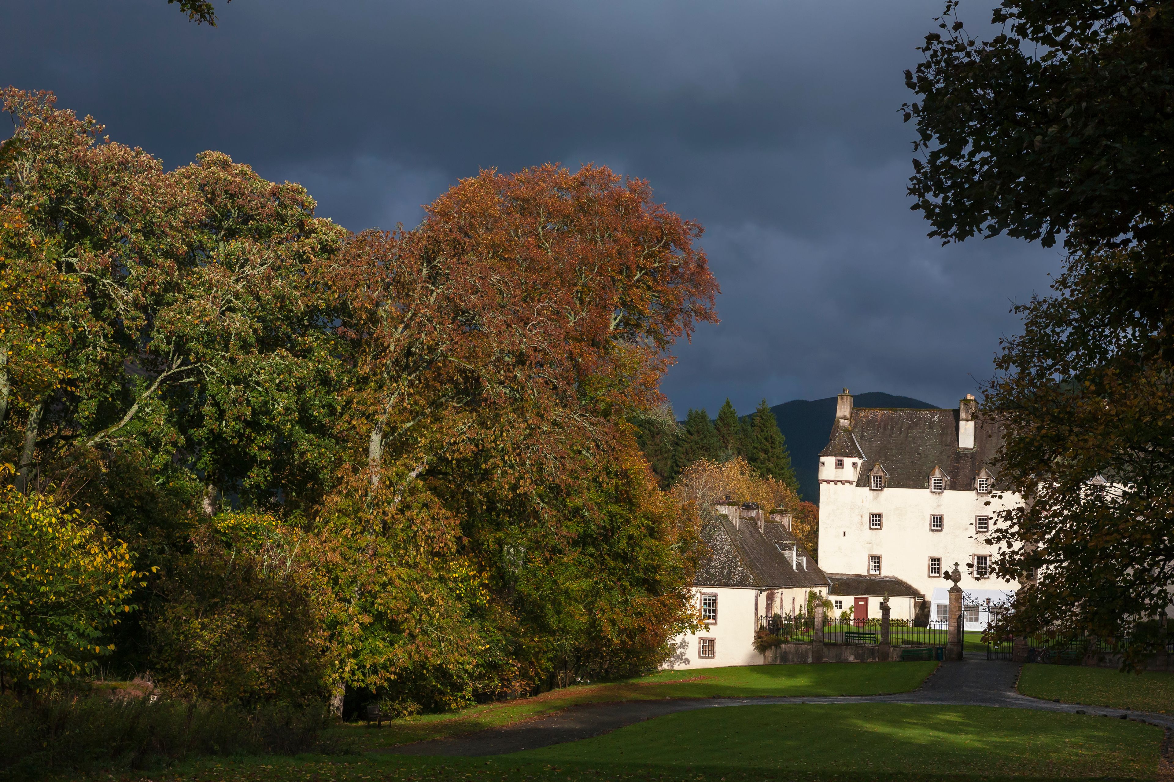 A large white building with a dark roof, surrounded by trees with autumn foliage.