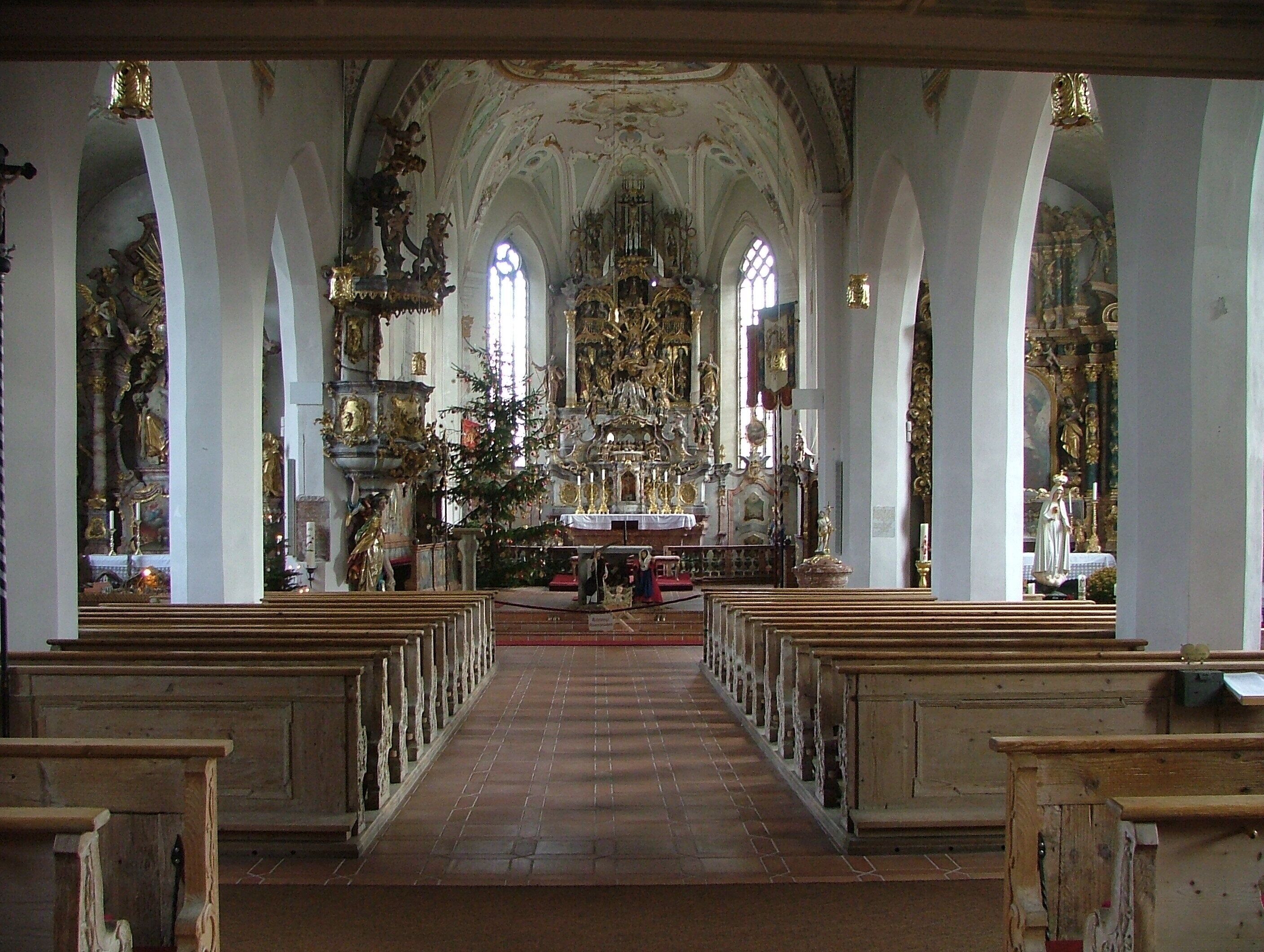 An ornate church interior with high ceilings, arched windows, and a central altar adorned with religious statues and decorations.