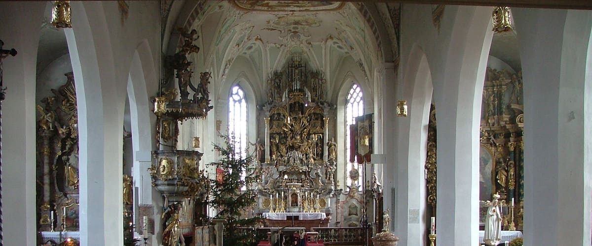 An ornate church interior with high ceilings, arched windows, and a central altar adorned with religious statues and decorations.