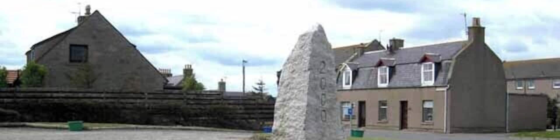 A stone monument in a grassy area with a building in the background.