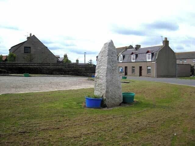 A stone monument in a grassy area with a building in the background.