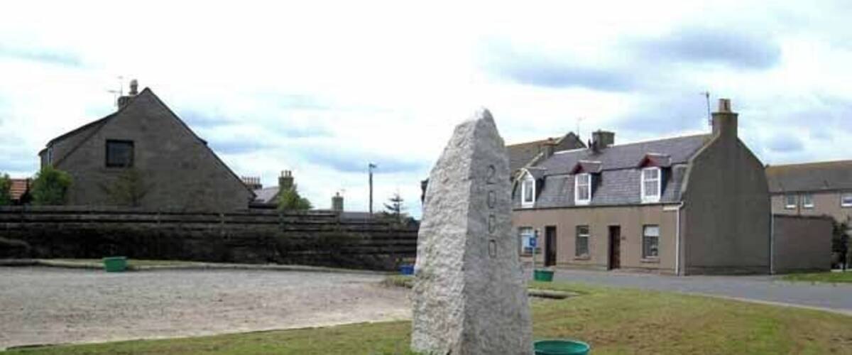 A stone monument in a grassy area with a building in the background.