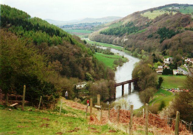 A river flowing through a valley with a bridge, surrounded by hills and greenery.