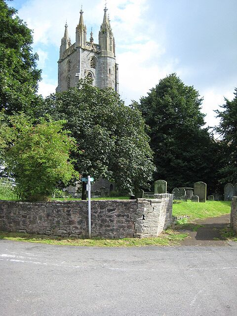 A church with a tall tower, surrounded by trees and a stone wall.