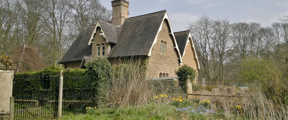 A stone house with a steeply pitched roof, surrounded by a garden with daffodils and other wildflowers.