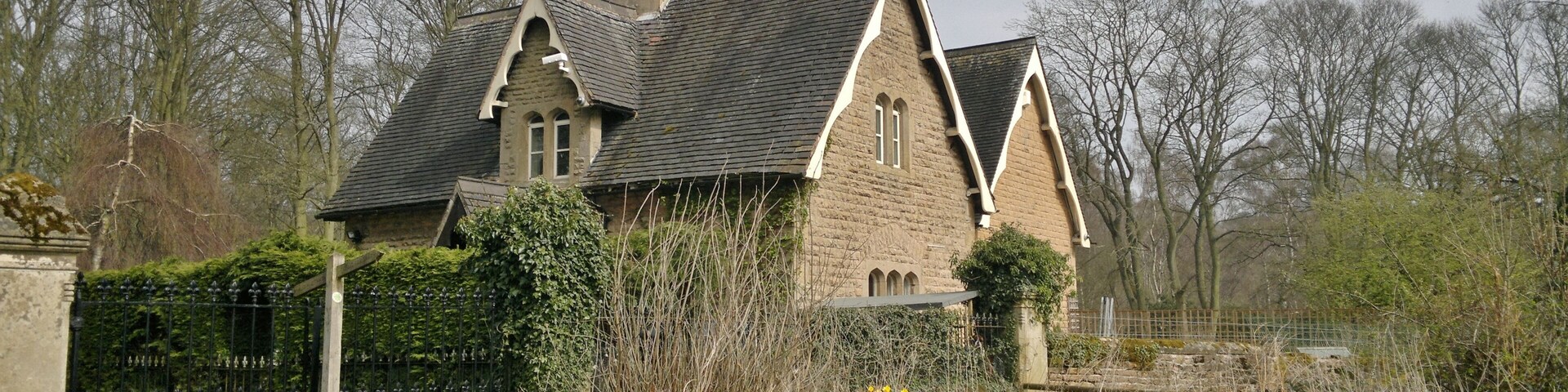 A stone house with a steeply pitched roof, surrounded by a garden with daffodils and other wildflowers.