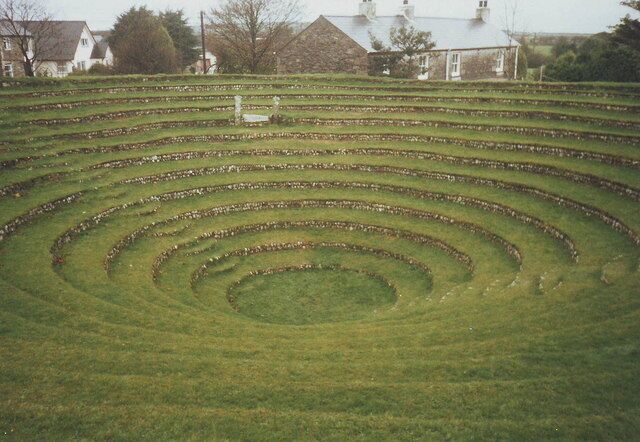 Un gran laberinto en espiral en un campo cubierto de hierba, con casas al fondo.