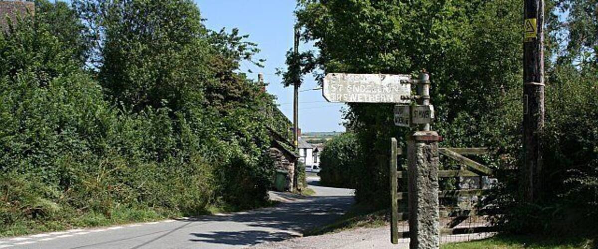 A rural road with a directional signpost and a stone pillar.