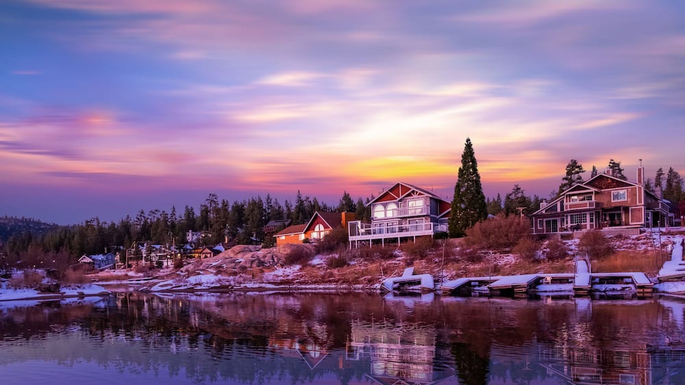 A lakeside community with houses, a dock, and a sunset.