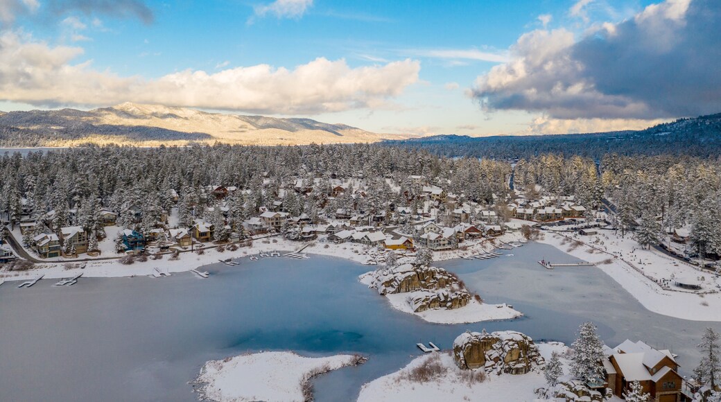 Aerial view of Big Bear Lake and town in California with the lake frozen on a sunny blue sky day in the Winter with pine trees below.