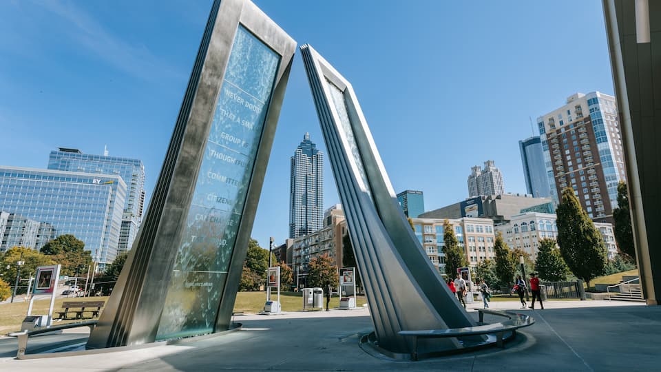 Een modern sculptuur in een stadspark, met hoge gebouwen op de achtergrond.