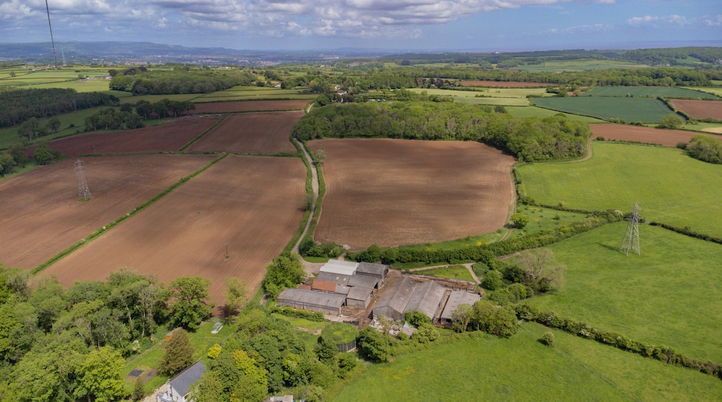 A rural landscape with fields, a small cluster of buildings, and distant hills.