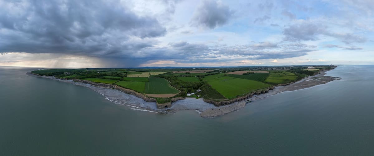 An aerial view of a coastal landscape with fields, a beach, and a stormy sky.