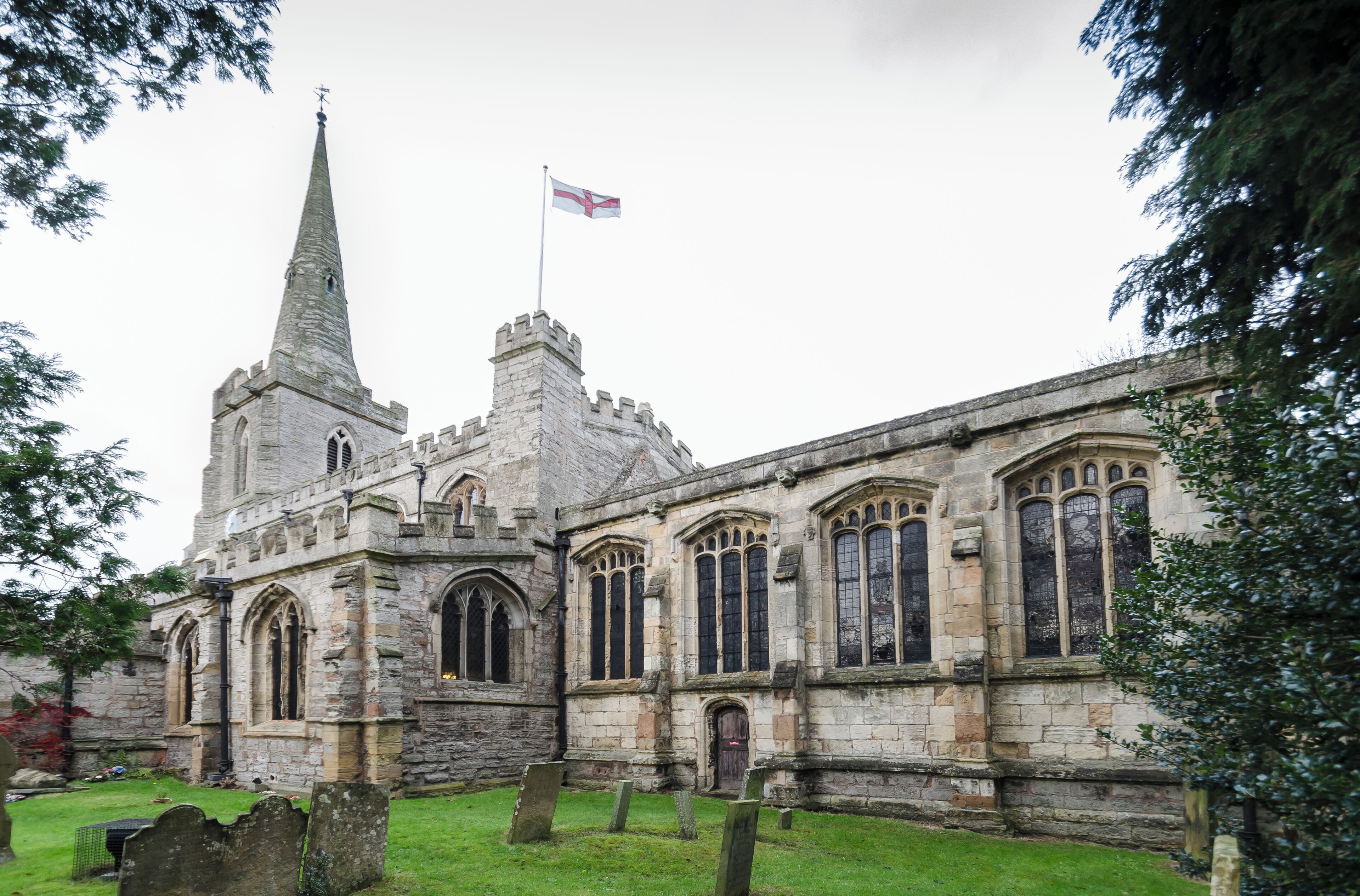 A historic stone church with a tall spire and a flag.