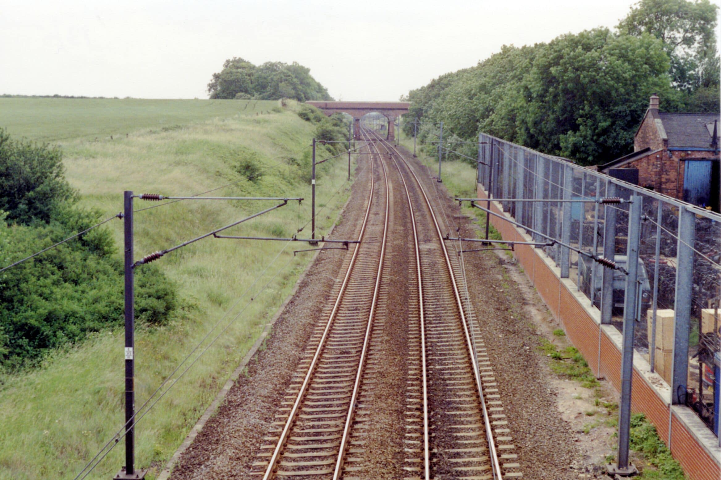 Southward up the ECML at site of Tuxford North station, 1992. View up the ex-GNR Doncaster - London section of the East Coast Main Line, electrified 1989. Nothing is left of the station, which closed 4/7/55 to passengers, 15/6/64 to goods. Just beyond the bridge ahead there had been a loop to the west connecting with the ex-GCR (Lancashire, Derbyshire & East Coast) line, which crosses the ECML shortly beyond at the former Dukeries Junction station