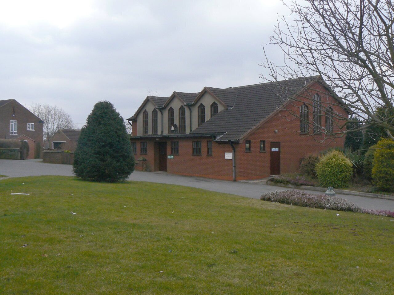 A brick building with a sloped roof, surrounded by a grassy area and a few trees.