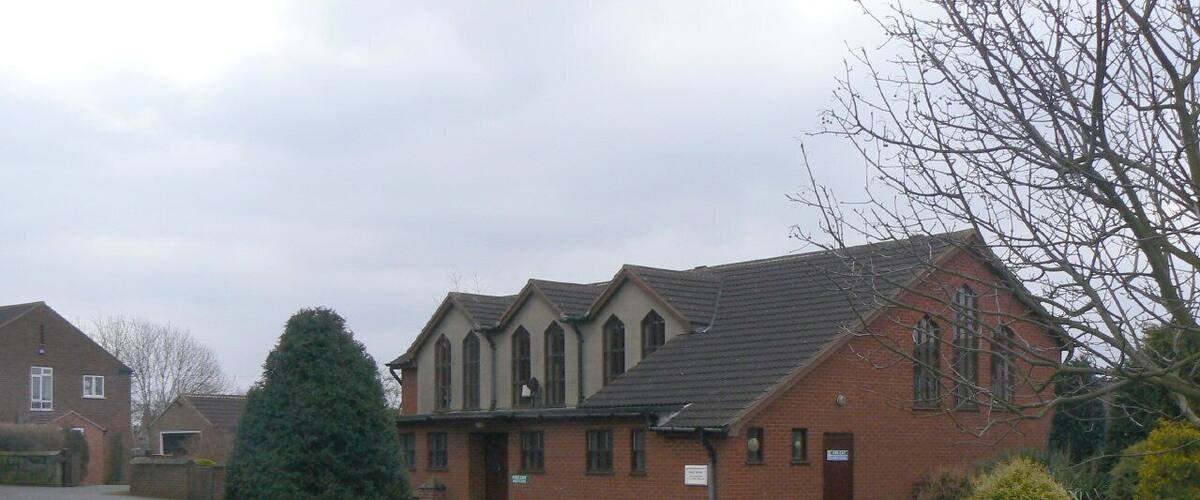 A brick building with a sloped roof, surrounded by a grassy area and a few trees.