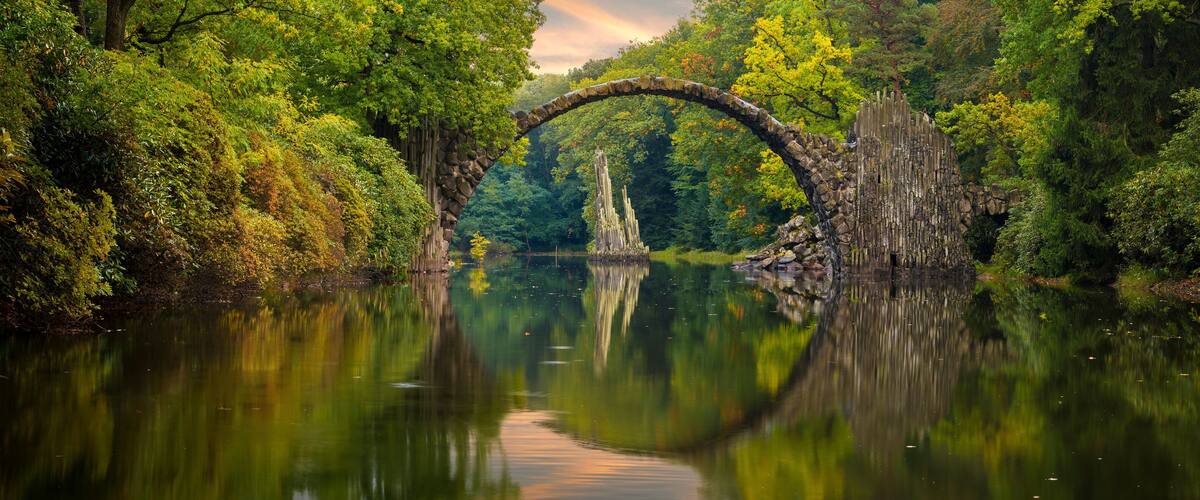 A stone arch bridge over a calm river surrounded by lush greenery.