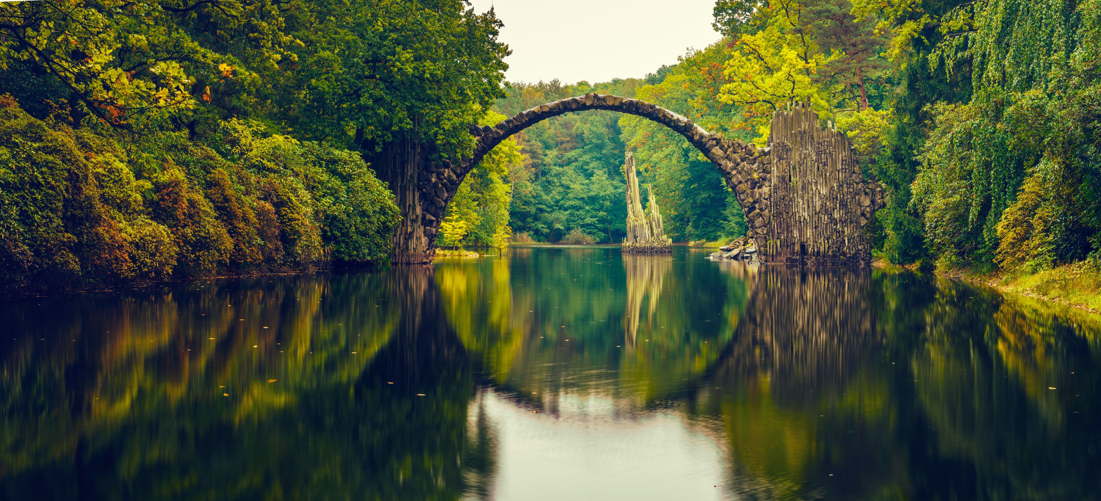 A stone arch bridge over a calm river surrounded by dense forest.