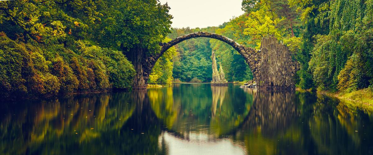 A stone arch bridge over a calm river surrounded by dense forest.