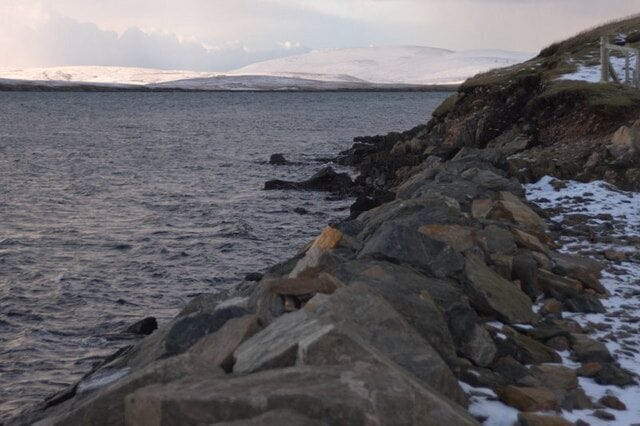 Coastline at Ulsta In the foreground are the reinforcements for the coast beside the Yell Sound ferry terminal at Ulsta. In the background, is a snow-covered Ronas Hill, the highest point in Shetland at 450m.