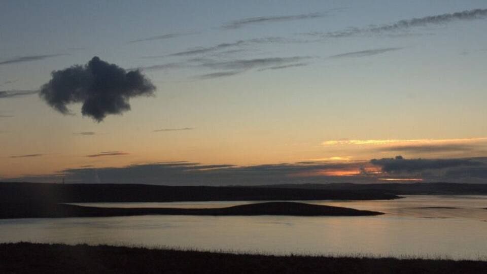 A sunset over a calm lake with a small island in the center.