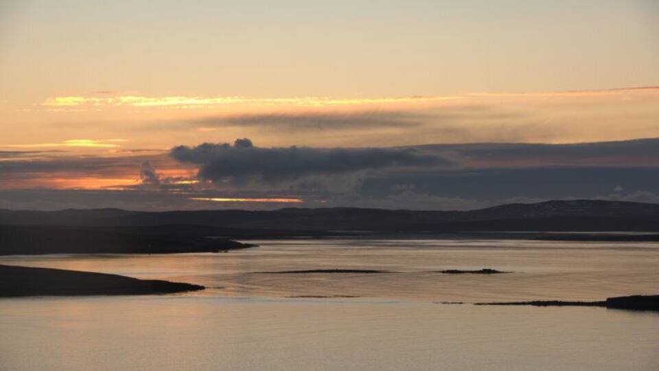 A calm lake at sunset with silhouettes of hills in the background.