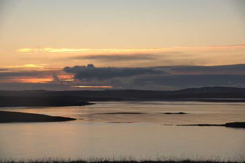 A calm lake at sunset with silhouettes of hills in the background.