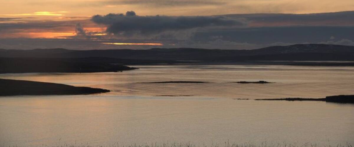 A calm lake at sunset with silhouettes of hills in the background.