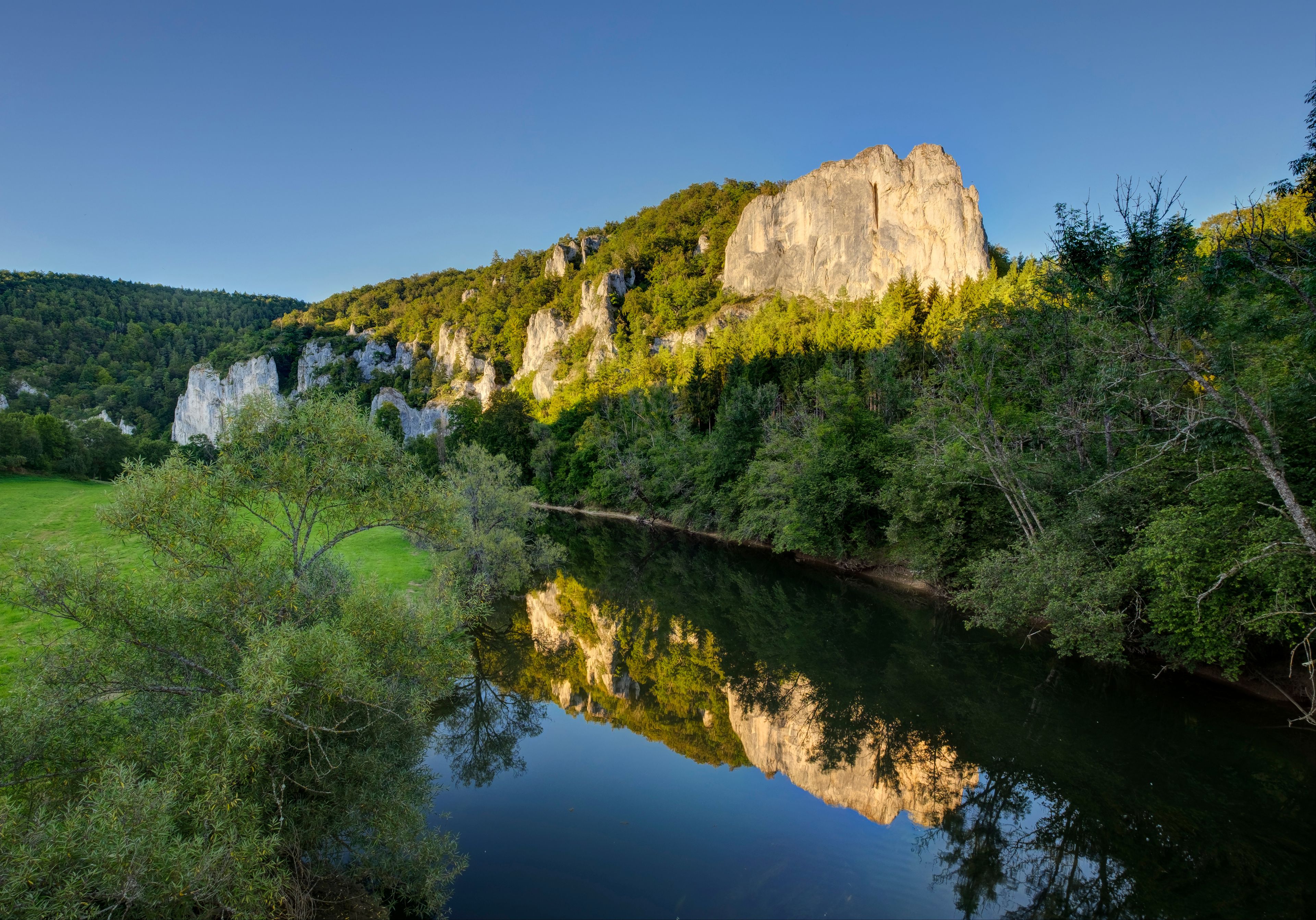 A river reflecting a rocky hill with dense forest.