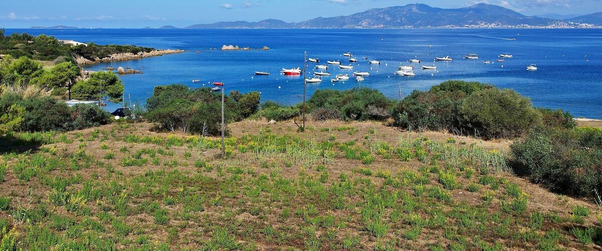A coastal landscape with boats on the water, greenery, and distant mountains.