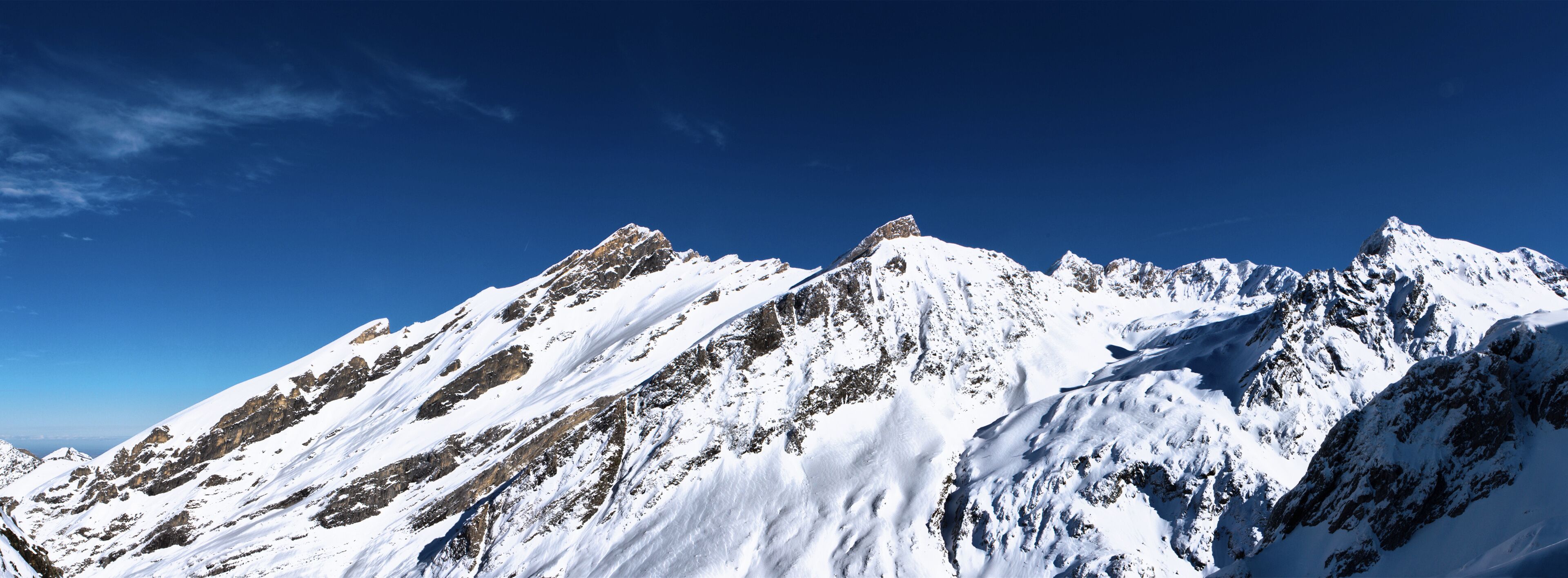 A snow-covered mountain range with sharp peaks under a clear blue sky.