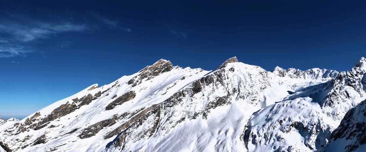 A snow-covered mountain range with sharp peaks under a clear blue sky.