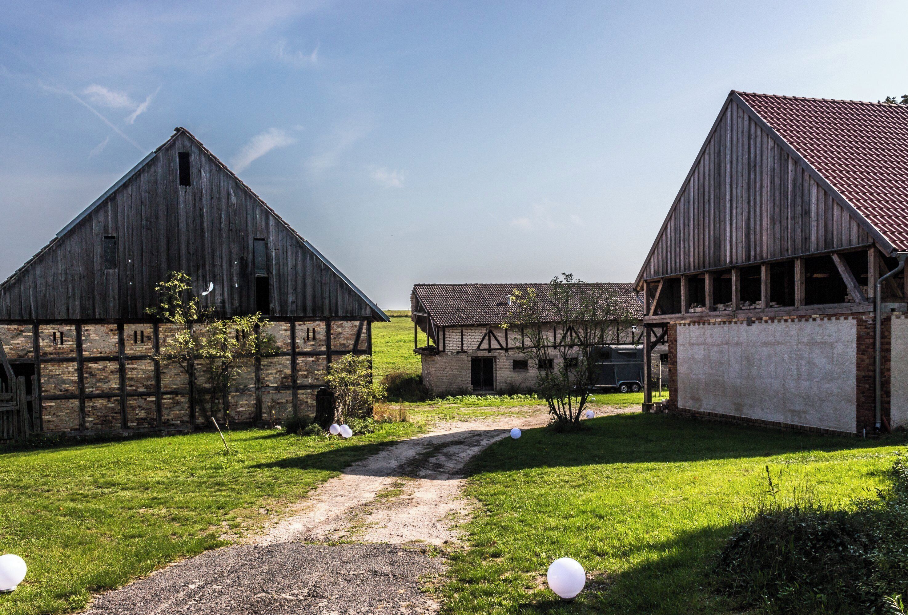 A rural landscape with two barns, a dirt path, and green fields.
